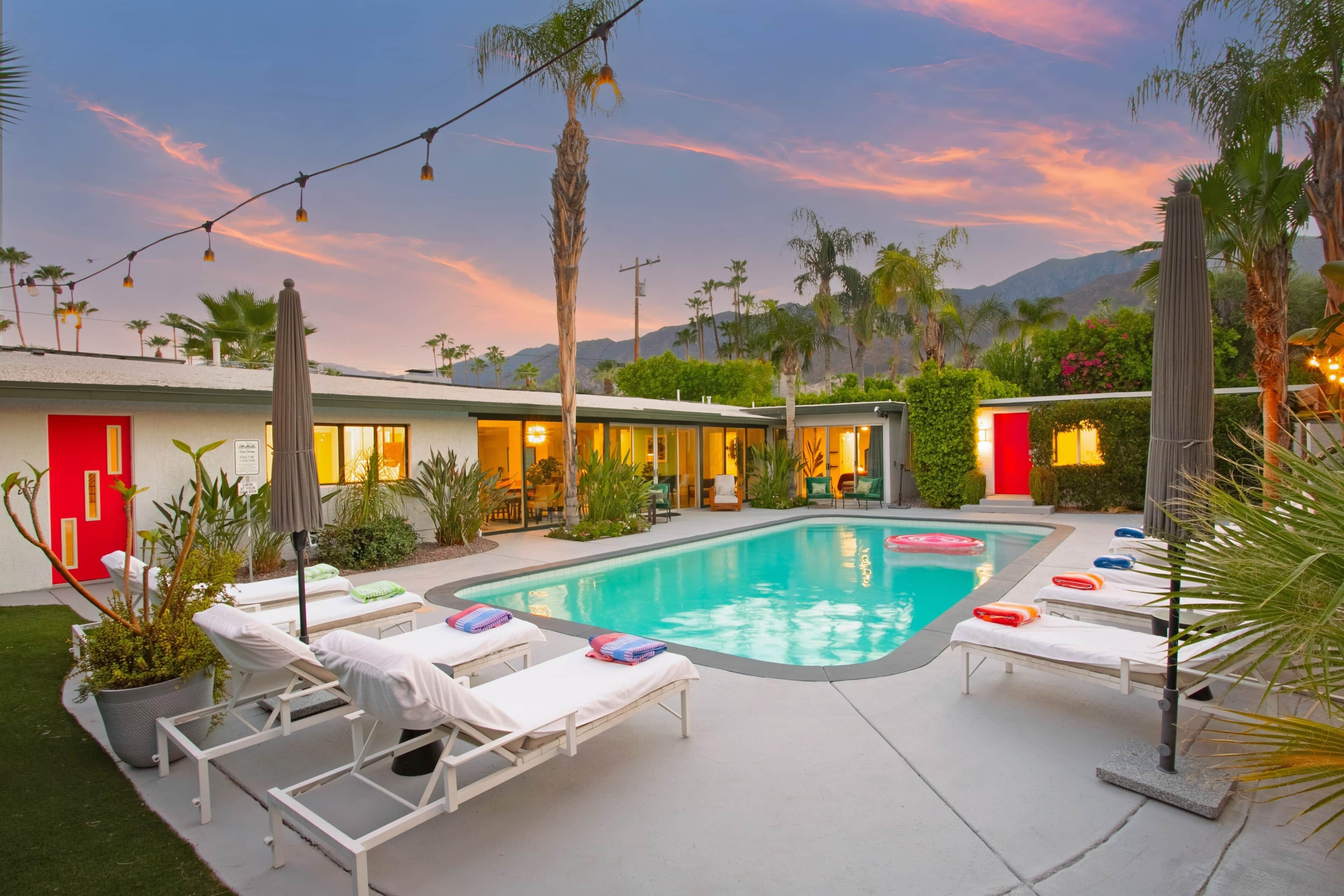 A swimming pool with lounge chairs, a red door, and a mountain backdrop.