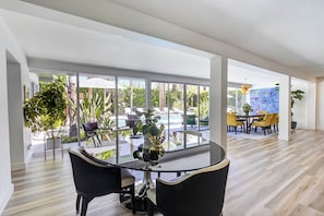 Une pièce spacieuse avec un grand mur de verre, une table ronde entourée de chaises et une vue sur un espace piscine extérieur.