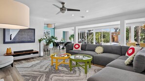 A modern living room with a grey sofa, two round coffee tables, a TV on a wooden stand, and a ceiling fan. - Casa Del Sol, a private Palm Springs Oasis (Palm Springs)