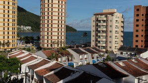 A coastal urban area with a mix of modern and traditional buildings, including a prominent cylindrical structure and several multi-story buildings with balconies. - Apartamento aconchegante - Caraguatatuba (Caraguatatuba)