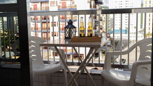 A balcony with two white plastic chairs, a small table, and two bottles of Corona Extra beer. - Apartamento aconchegante - Caraguatatuba (Caraguatatuba)