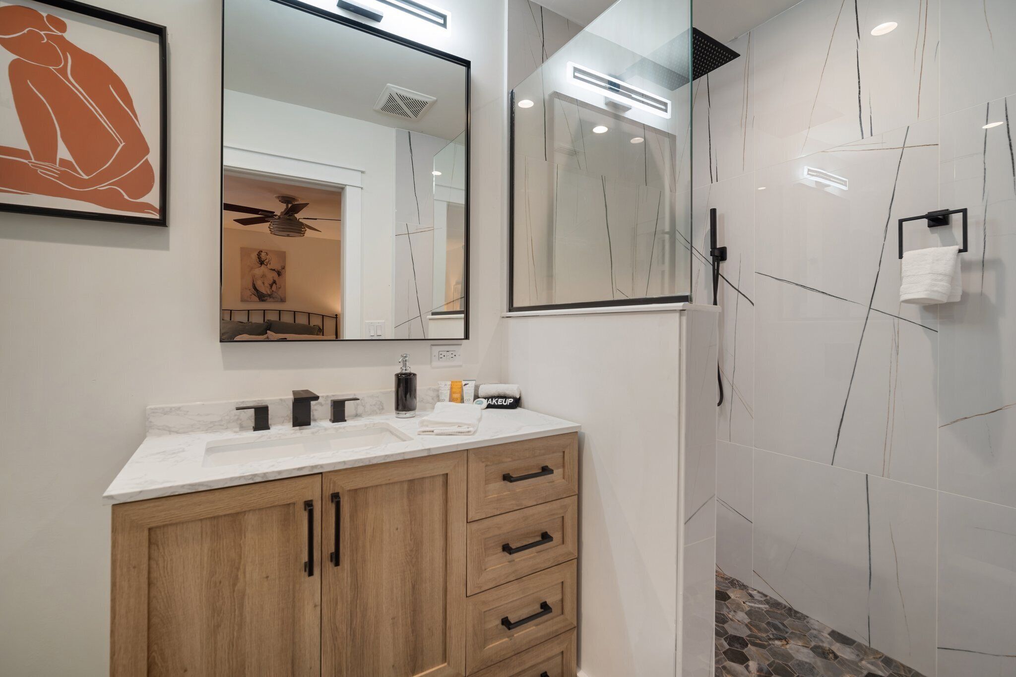 A modern bathroom with a wooden vanity, a large mirror, and a glass shower enclosure.