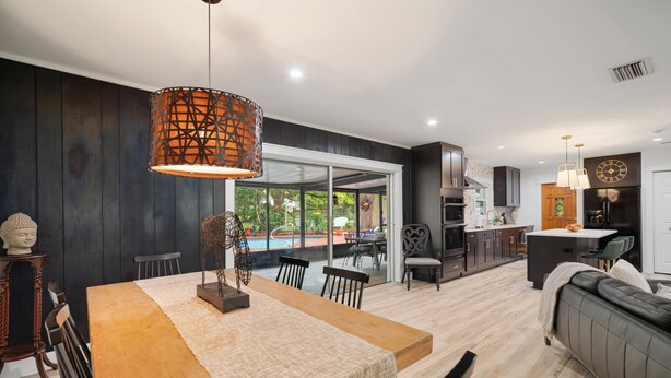 A modern kitchen with dark cabinetry, a central island, and a dining area with a wooden table and chairs.
