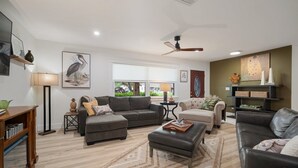 A modern living room with a grey sectional sofa, a leather armchair, and a coffee table. There is a floor lamp, a side table with a lamp, and artwork on the walls.