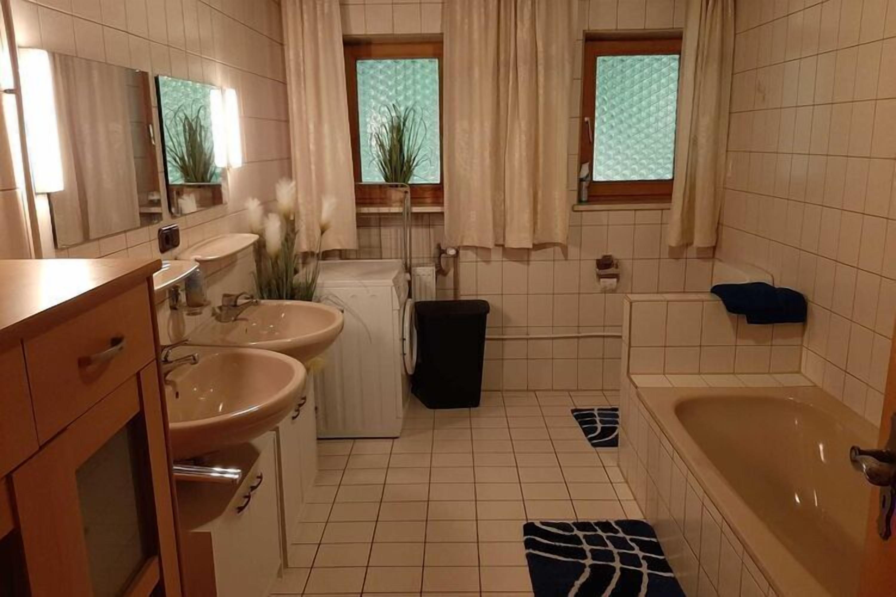 A bathroom with two sinks, a bathtub, and a window with curtains.