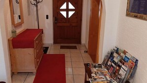 Ein Flur mit Holztür, Kleiderhaken, rotem Teppich und einem Tisch mit Zeitschriften.