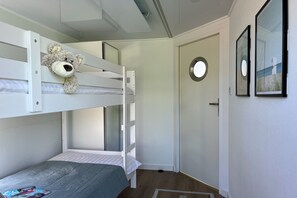 Une chambre avec un lit superposé, un ours en peluche posé sur le lit du haut, une porte dotée d’une fenêtre ronde et des tableaux encadrés accrochés au mur.