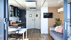 A modern interior with a dining area, a sofa, and a TV mounted on a wooden wall. - Houseboat in Łazy by Lake Jamno and Sea (Łazy)