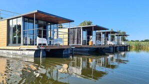 A modern floating house with glass walls, wooden deck, and white furniture. - Houseboat in Łazy by Lake Jamno and Sea (Łazy)