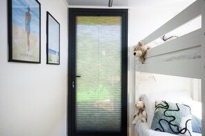 Une chambre avec un lit superposé, une porte dotée d’un panneau en verre dépoli et deux tableaux encadrés accrochés au mur.