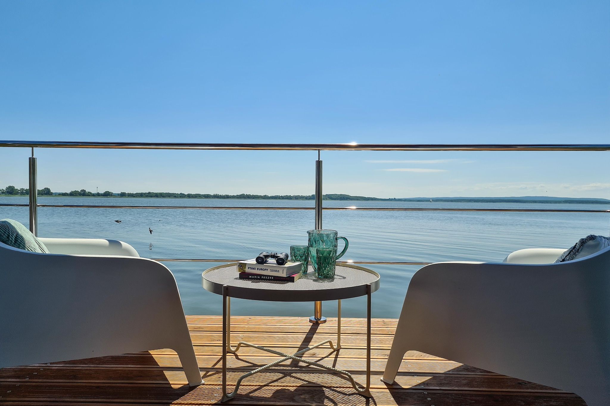 Una terraza con dos sillas, una mesa y vista a un cuerpo de agua tranquilo.