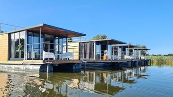 Une maison flottante moderne avec des murs en verre, une terrasse et un espace salon couvert.