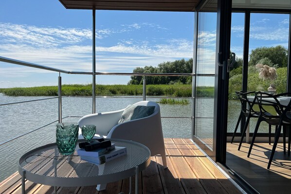 A deck with a table and chairs, overlooking a body of water and greenery.