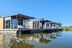 A modern floating house with glass walls, a deck, and a covered seating area. - Houseboat in Łazy near Baltic Sea & Lake Jamno (Łazy)