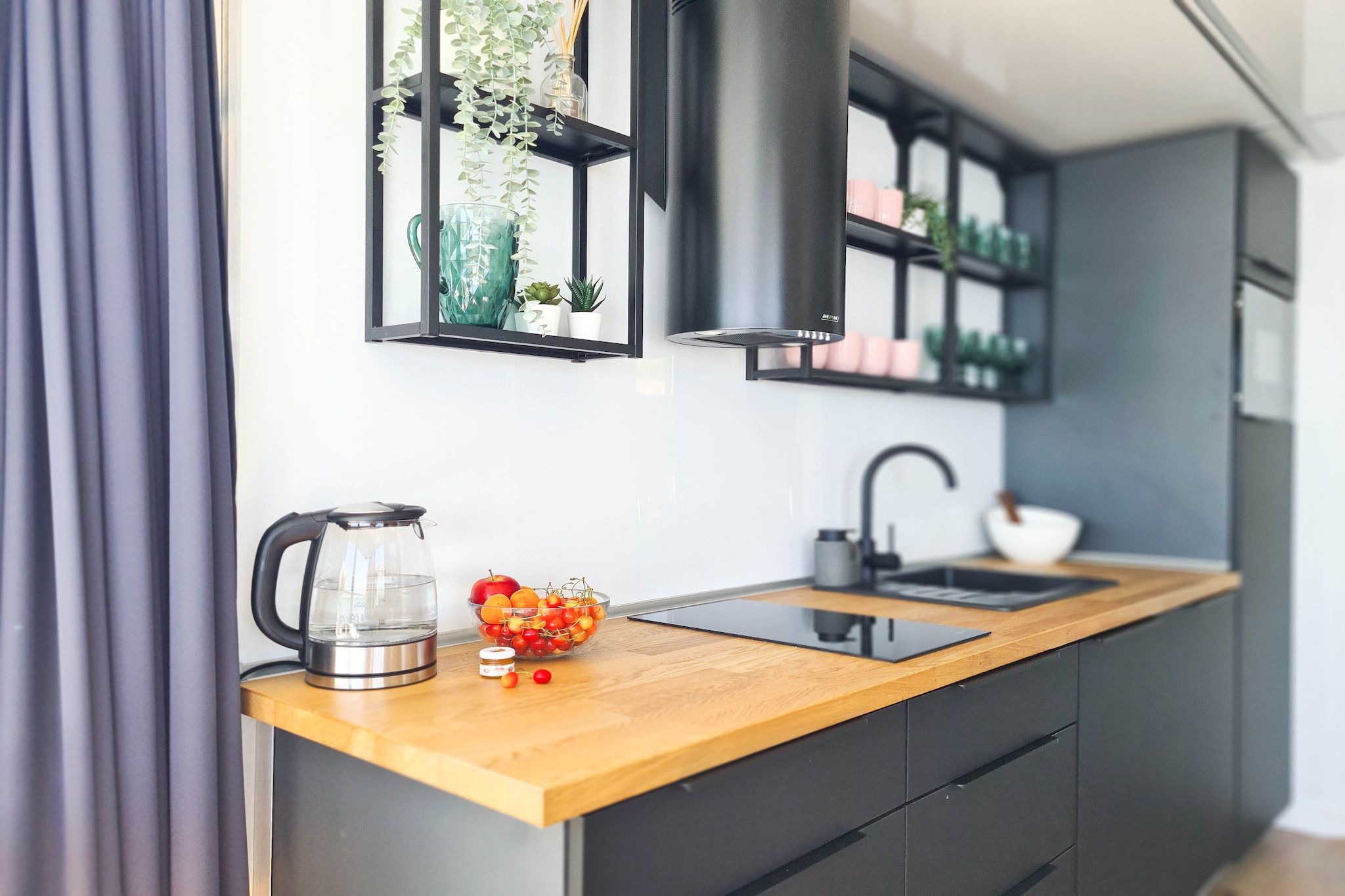 Een moderne keuken met een houten aanrecht, een waterkoker, een schaal met fruit en een zwarte afzuigkap.