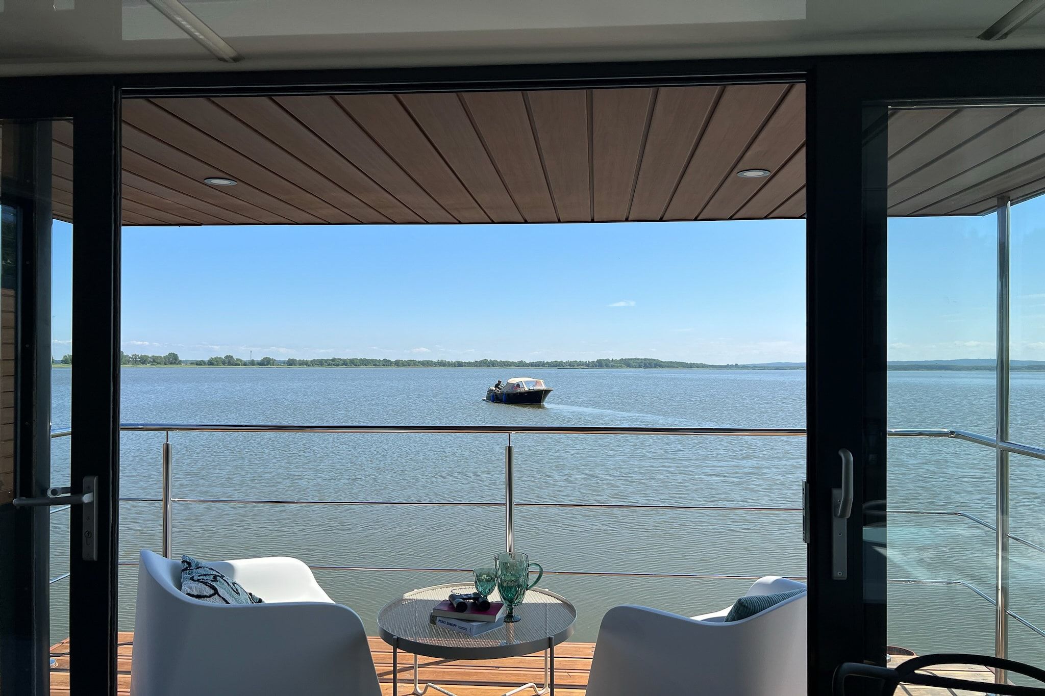 Ein Balkon mit Seeblick, ein Boot in der Ferne und ein Tisch mit Buch und Gläsern.