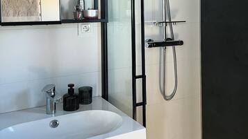 Un baño con lavamanos blanco, un espejo y una ducha con cabezal de ducha manual.