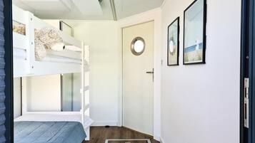 A room with bunk beds, a door with a round mirror, and framed pictures on the wall.