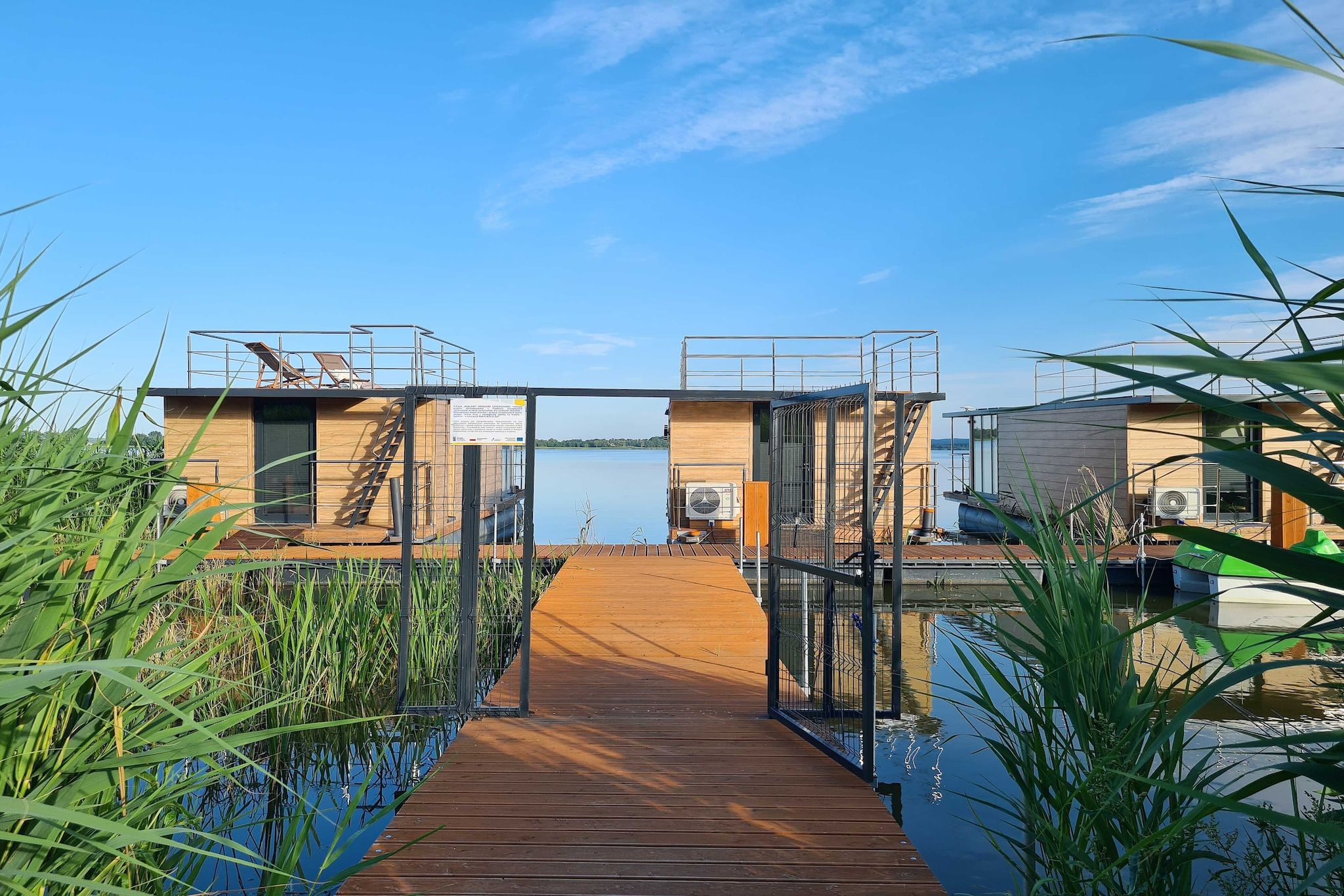 Un muelle de madera que conduce a un edificio con barandilla metálica y vistas al agua.
