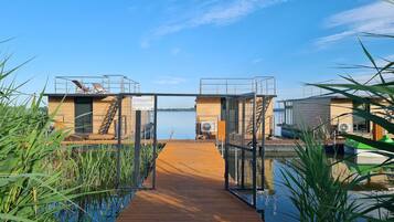 Un muelle de madera que conduce a un edificio con barandilla metálica y vistas al agua.