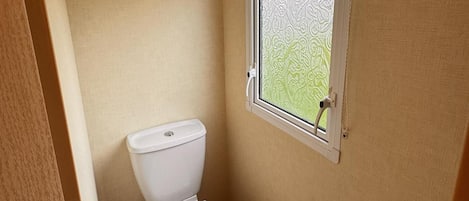A small, compact bathroom with a toilet, a window with frosted glass, and a towel ring on the wall.