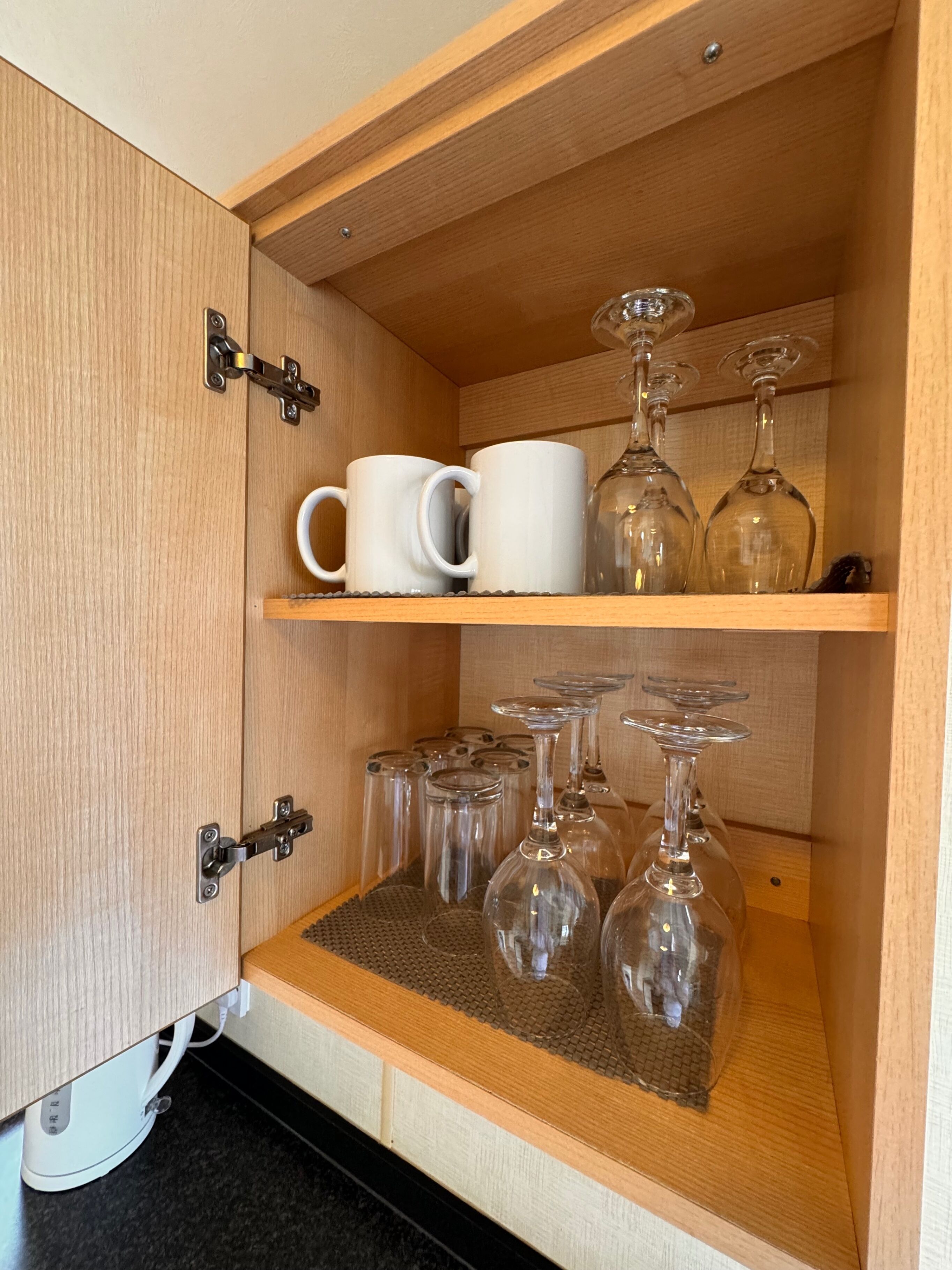 Un meuble en bois doté de deux étagères : l’une contient des tasses blanches et l’autre, des verres à vin.