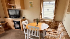 Een compacte leefruimte met een kitchenette, een televisie, een eettafel met stoelen en een bank.