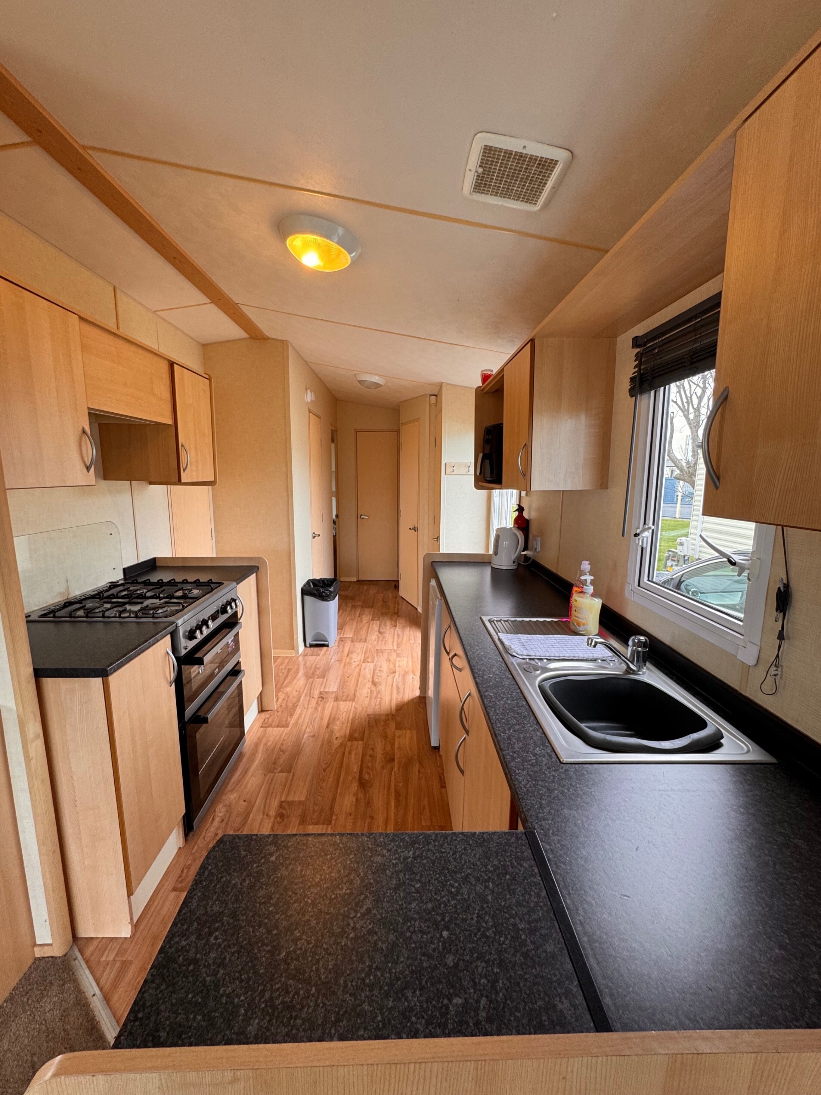 A compact kitchen with wooden cabinets, a gas stove, a sink, and a window with a view.