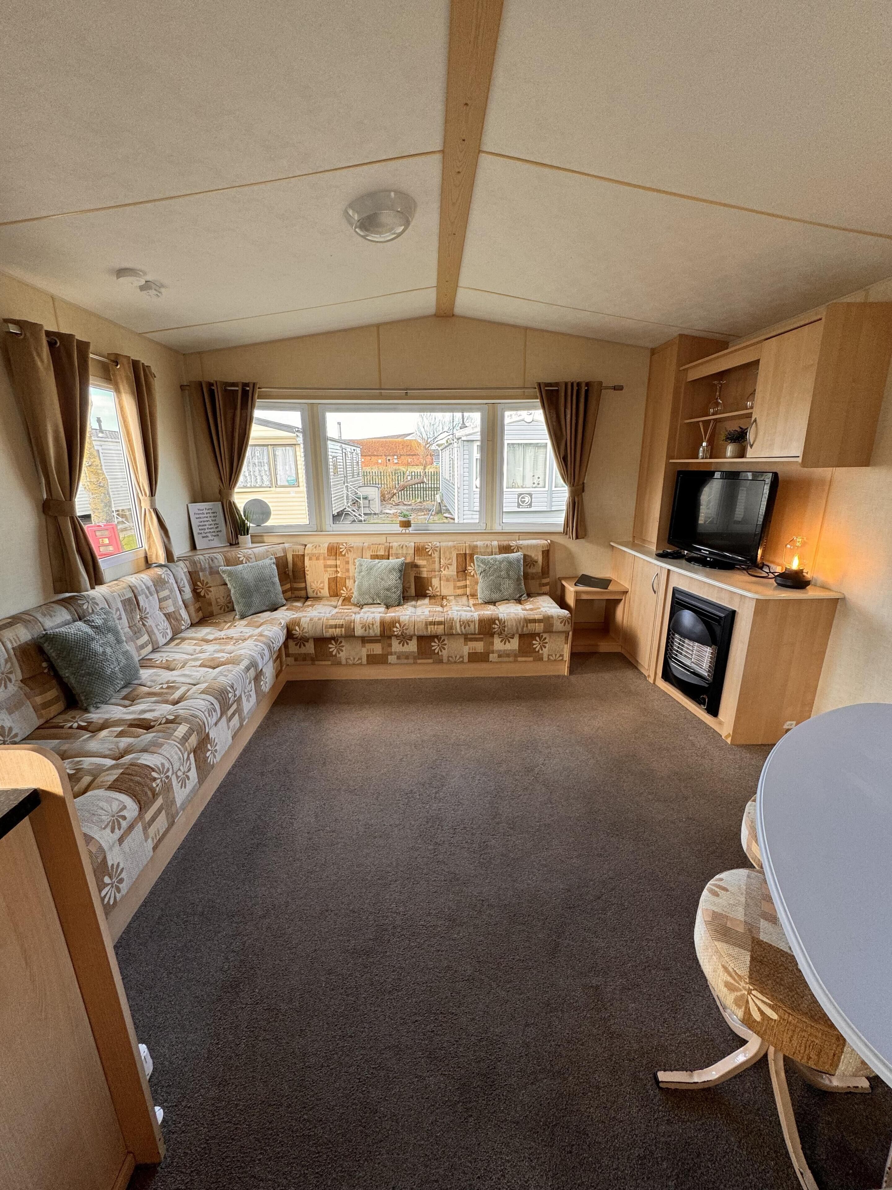 A cozy RV interior with a sofa, a small table, a TV, and a kitchenette area.
