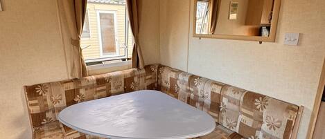 A compact living space with a round table, two cushioned chairs, a window with curtains, and a mirror on the wall.
