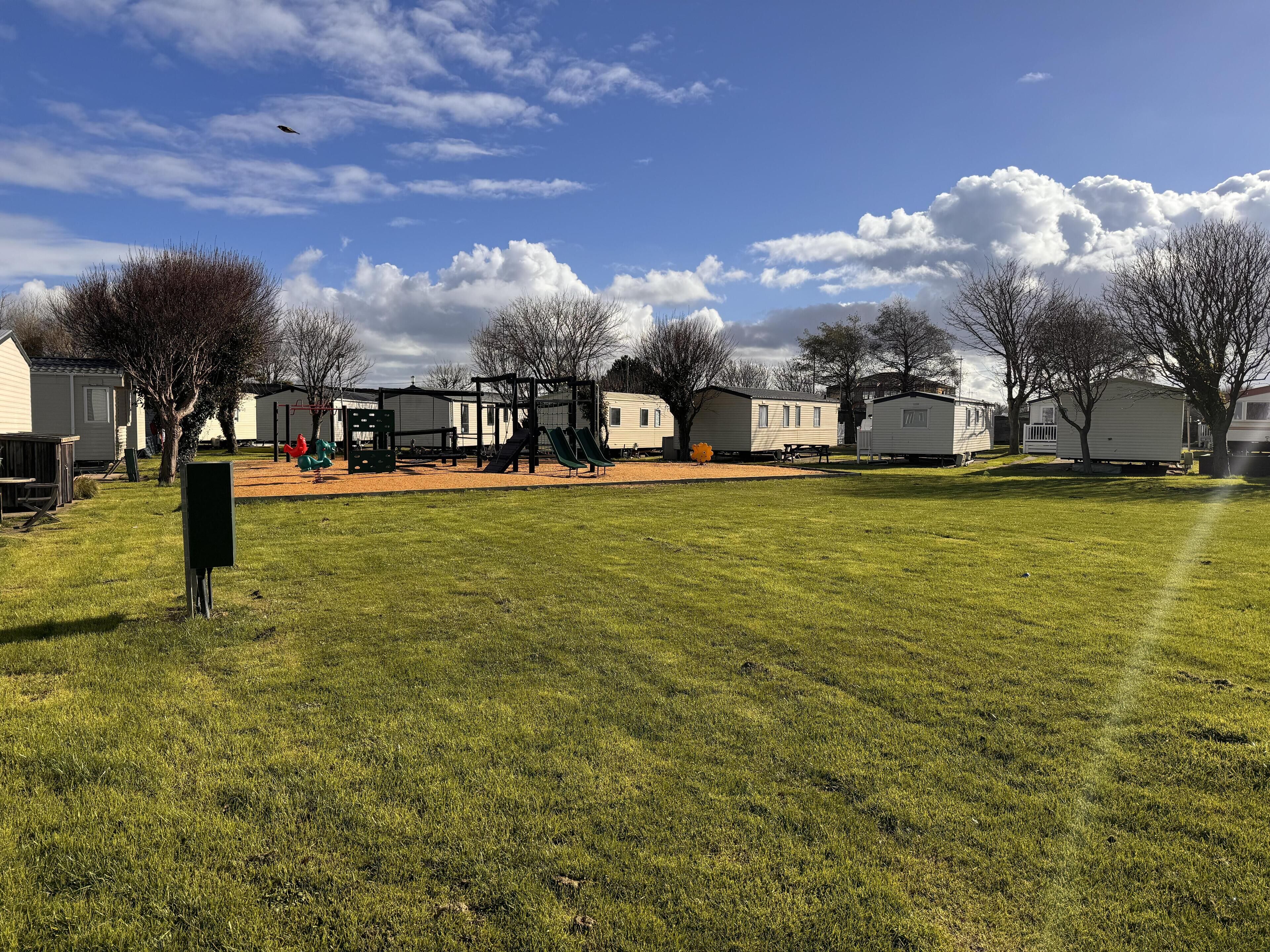 A grassy area with a playground, mobile homes, and trees.