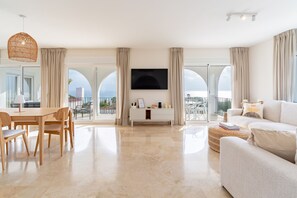 Ein geräumiges Wohnzimmer mit großem Flachbildfernseher, einem Essbereich mit Holzmöbeln und großen Fenstern mit Blick auf die Stadt.