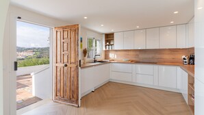 Eine moderne Küche mit weißen Schränken, einer Holz Arbeitsplatte und Blick auf eine Stadtlandschaft durch eine offene Tür.
