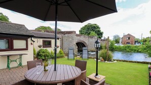 A patio with wicker furniture, a table, and an umbrella. - River Cottage (Penrith)