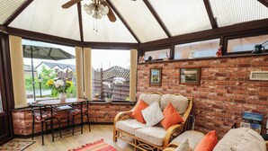 A cozy room with a brick wall, a wooden ceiling, a wicker sofa, a dining table, and a view of the outdoors. - River Cottage (Penrith)