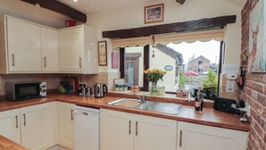 A kitchen with white cabinets, a microwave, a sink, and a window with a view of the outside. - River Cottage (Penrith)