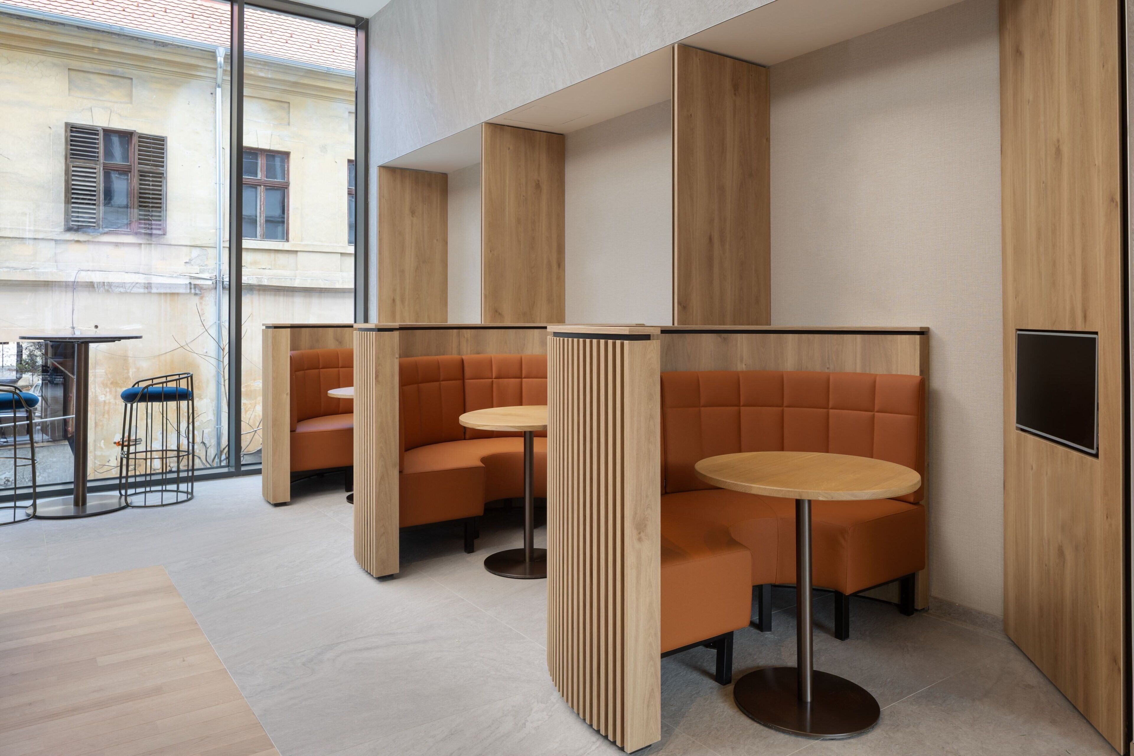 Un interior moderno con separadores de madera, asientos con cojines naranja y mesas redondas.