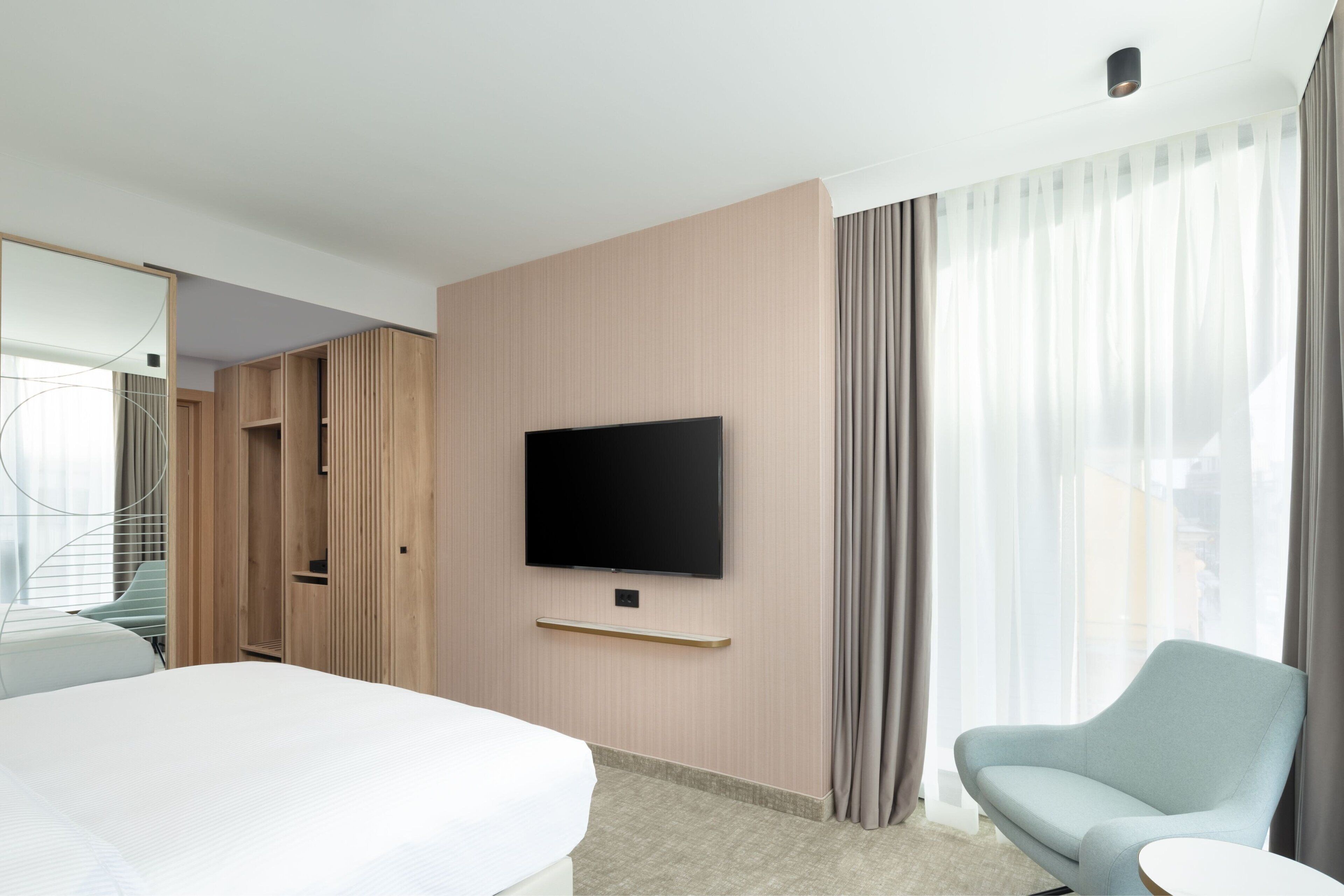 Habitación de hotel con cama, televisión montada en la pared, zona de estar con una silla y un armario.