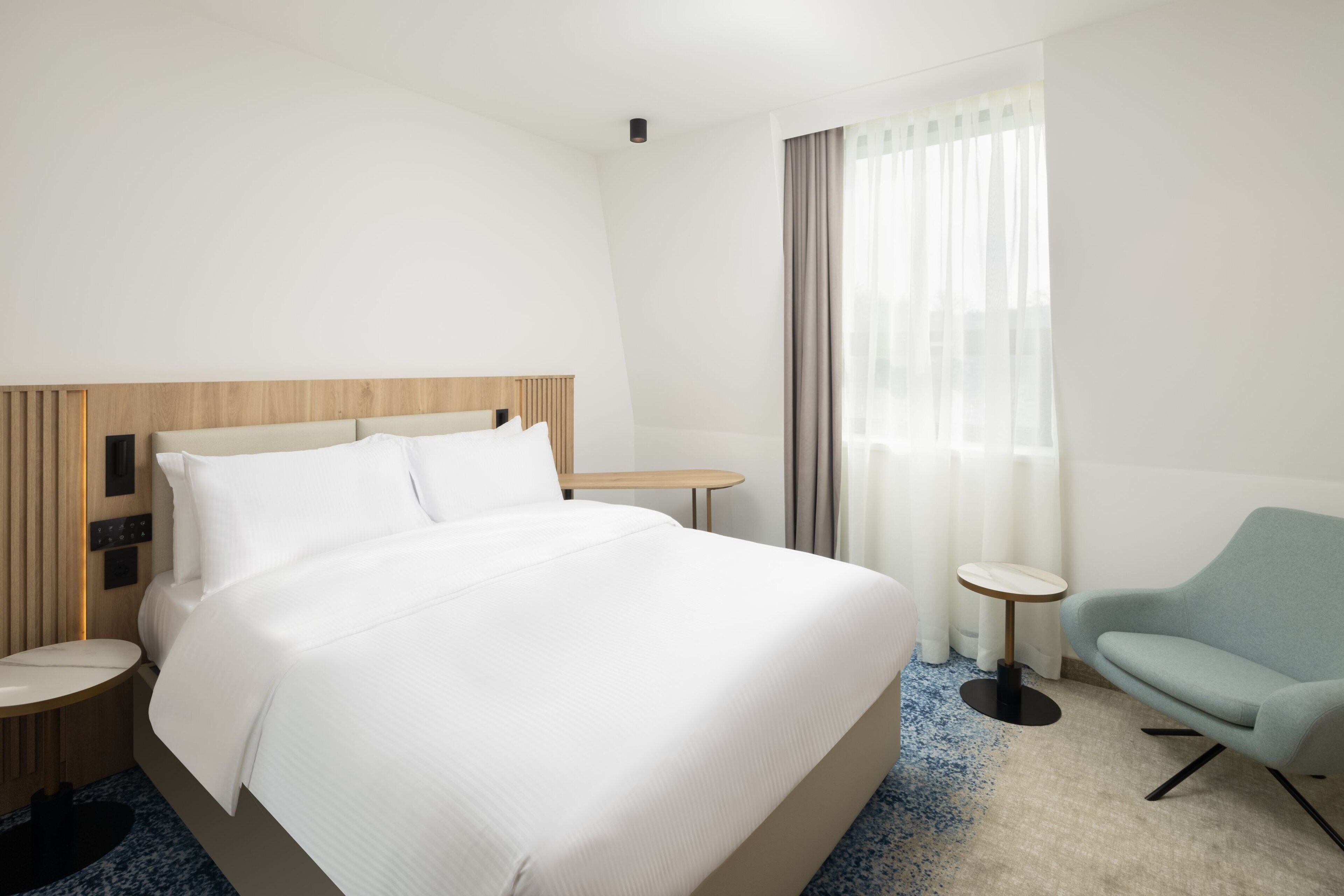 Une chambre d’hôtel avec un grand lit, une petite table ronde, une chaise et une fenêtre avec des rideaux.