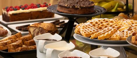 A buffet with various desserts like cakes, waffles, and pastries.