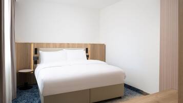 A modern hotel room with a large bed, a bedside table, and a small round table.