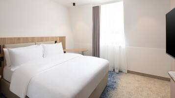 Quarto de hotel com uma cama grande, mesa de cabeceira, televisão de tela plana e janela com cortinas.