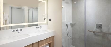 Un baño moderno con dos lavamanos, un espejo grande y una ducha con mampara de vidrio.