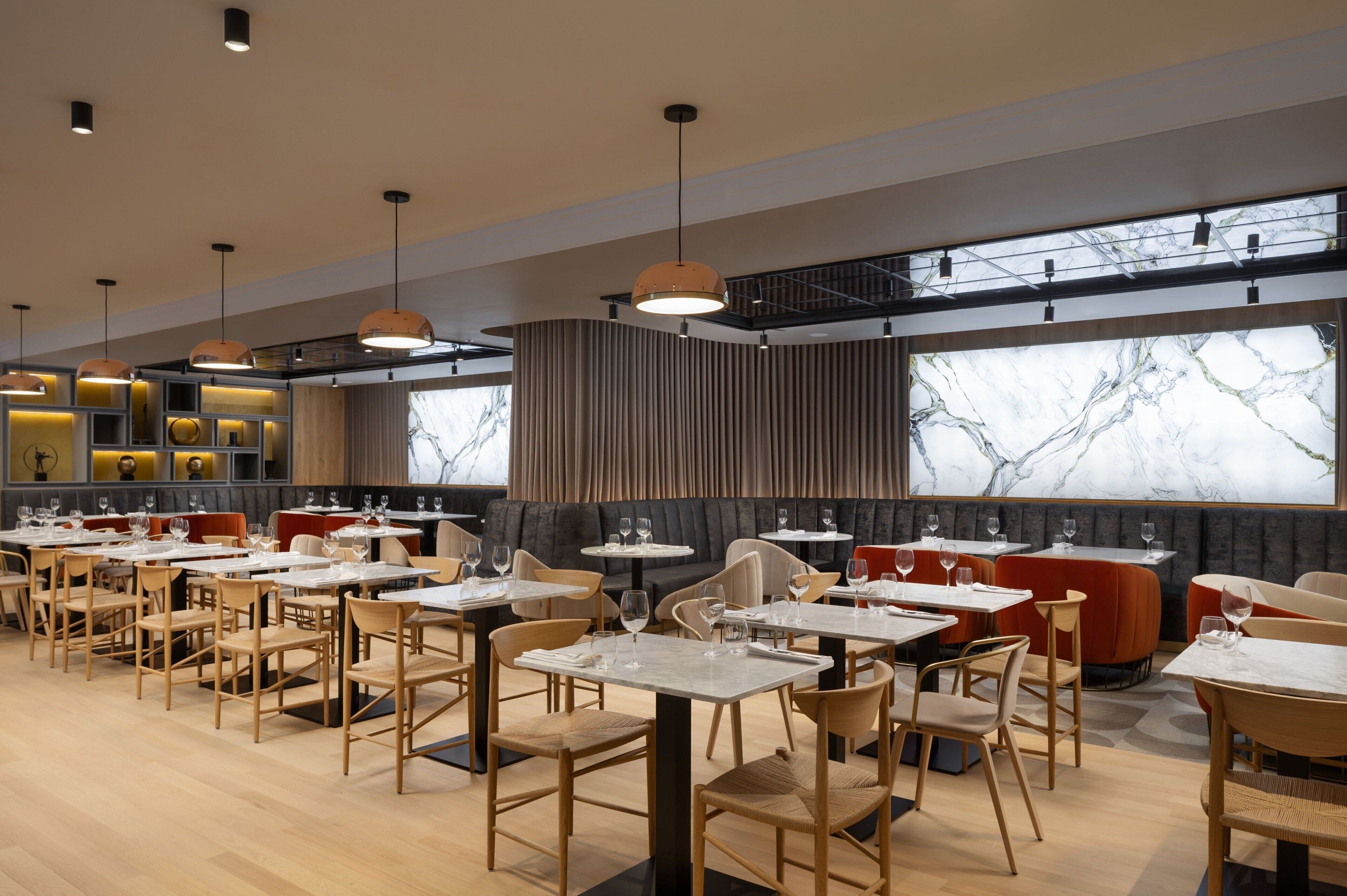 A modern restaurant with multiple dining tables and chairs, large windows with a view, and pendant lighting.