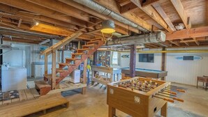 A spacious room with a wooden ceiling, a foosball table, and a pool table.