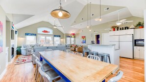 Une cuisine spacieuse dotée d’un îlot central, un coin repas avec une longue table en bois, et un espace salon confortable avec des canapés et des fauteuils.