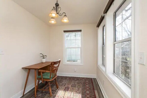 Un comedor con mesa y sillas de madera, un tapete estampado, una planta en maceta y una ventana con vistas.