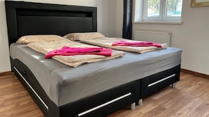 Un lit moderne avec une tête de lit noire, une literie grise et des serviettes roses.
