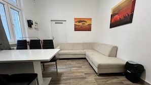 Un salon moderne avec un canapé d’angle blanc, une table à manger avec des chaises, un sac noir posé sur le sol et deux tableaux accrochés au mur.