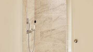 A walk-in shower with a handheld showerhead, a handheld shower attachment, and a wall-mounted control.